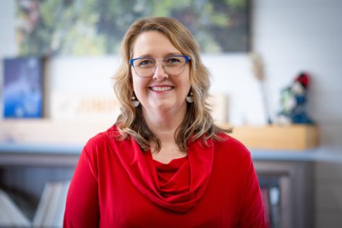 Woman in a red top with blonde hair and glasses smiles at camera
